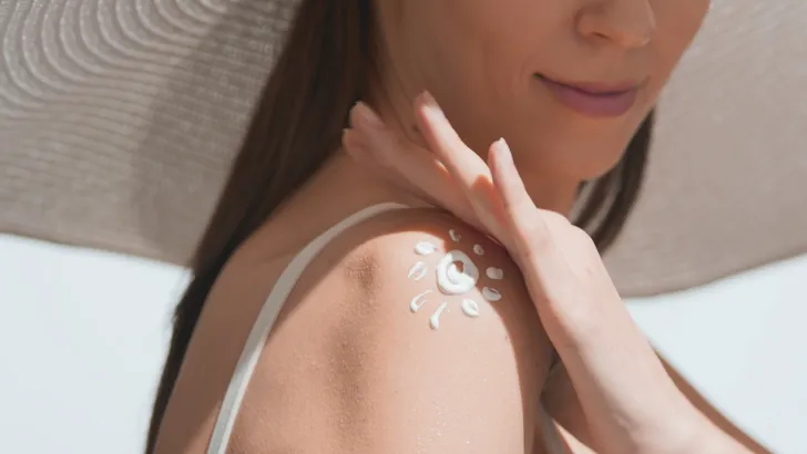 Foto van vrouw met SPF op schouder in de zon met grote hoed.