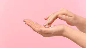 Vrouw die huidverzorging op haar handen aanbrengt op een gekleurde achtergrond.