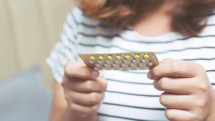 Woman hands opening birth control pills in hand on the bed in the bedroom. Eating Contraceptive Pill.