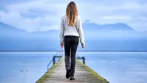 Young blond girl with long hair, standing from the back on a wooden pier
