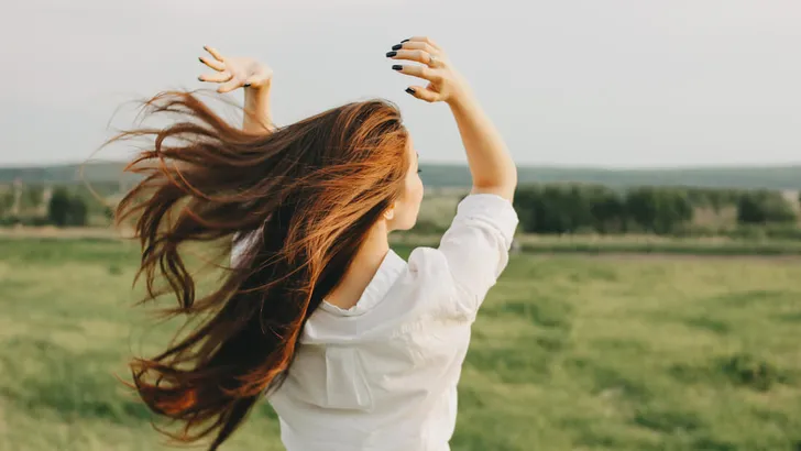 Close up portrait of beautiful carefree long hair girl in white clothes in field, view from back. Sensitivity to nature concept