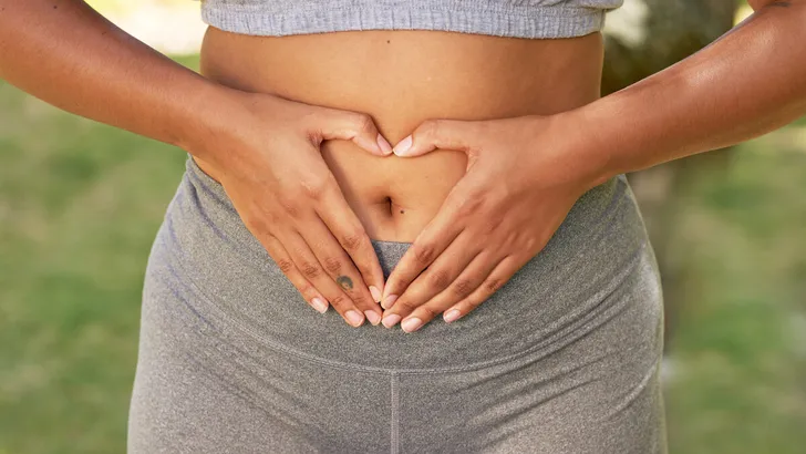 Close up of multi-ethnic woman holding hands in heart over belly, body positive