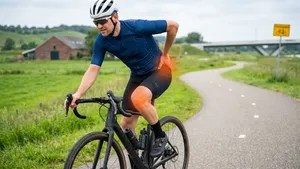 Een wielrenner in actie met een visuele rode gloed op zijn knie die de pijn symboliseert, de focus ligt op de knie en de crankarm van de fiets.