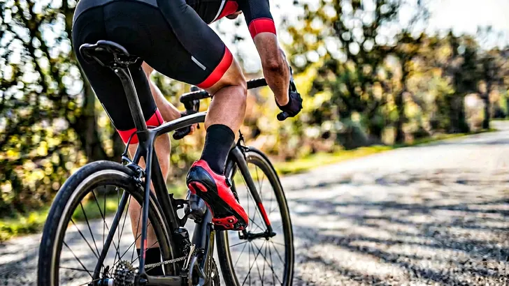Close-up van een rood schoenplaatje onder een racefietsschoen die is ingeklikt in het pedaal, de vaak over het hoofd geziene oorzaak van pijn aan de binnenkant van het bovenbeen tijdens het fietsen.