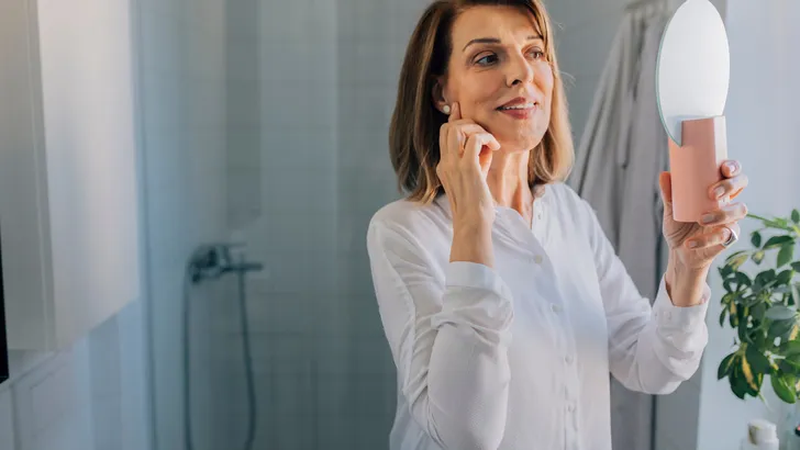 Anti Age Rituals: a Happy Mature Woman Looking at Herself in the Mirror in the Bathroom