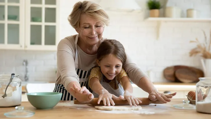 Aged grandma involve small grandkid in rolling dough with pin