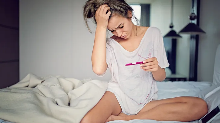 Shocked young girl with unwanted pregnancy looking the test in the bedroom