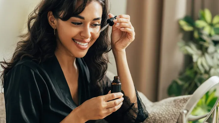 Young smiling woman sitting on a couch applying hyaluronic acid on a face