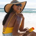 Smiling mixed race woman on beach holiday using sunscreen cream