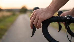 Close-up van de hand van een wielrenner op het stuur van een racefiets, waarbij de juiste techniek voor het vasthouden van de remhendel wordt getoond om slapende handen te voorkomen.