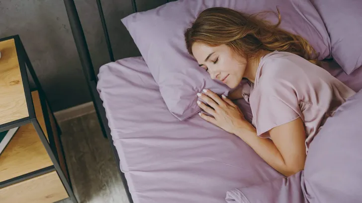 Top view young woman wear purple t-shirt pajama sleep lying in bed rest relax spend time in bedroom lounge home in own room hotel wake up dream be lost in reverie good mood day. Real estate concept.