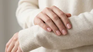 Verzorgde vrouwenhanden met een subtiele 'quiet luxury' manicure, rustend op een zachte crèmekleurige trui.