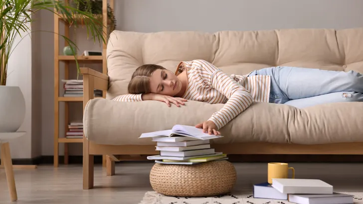 Young tired woman sleeping near books on couch at home