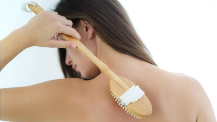 Een vrouw die haar rug borstelt in de douche