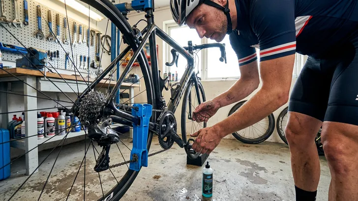 Een mannelijke wielrenner met helm reinigt de ketting van zijn racefiets met een kettingreiniger tool in z'n garage