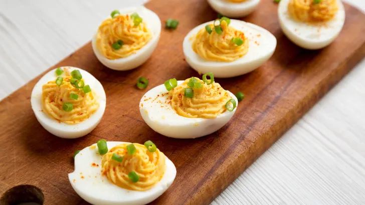 Homemade Deviled Eggs with Chives on a rustic wooden board on a white wooden background, low angle view. Close-up.