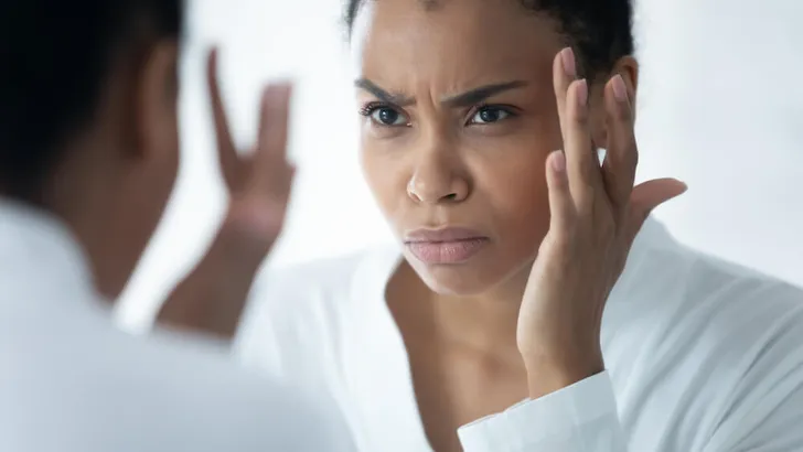 African woman looking in mirror see mimic wrinkles feels stressed