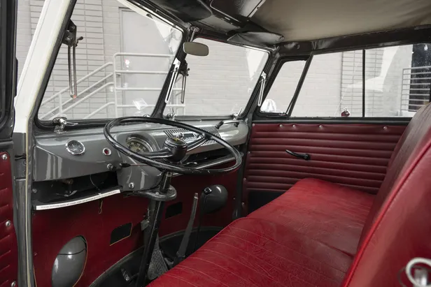 Cabine van de Volkswagen-bus met rood vinyl interieur, grijze dashboard en groot zwart stuur.
