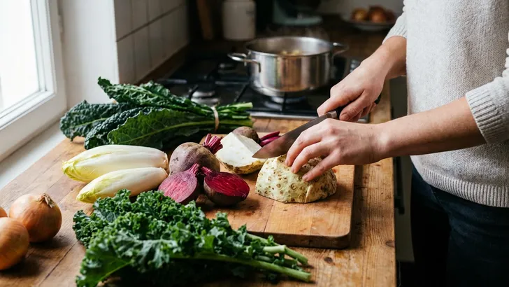 Vrouw snijdt wintergroenten op een houten keukenblad.