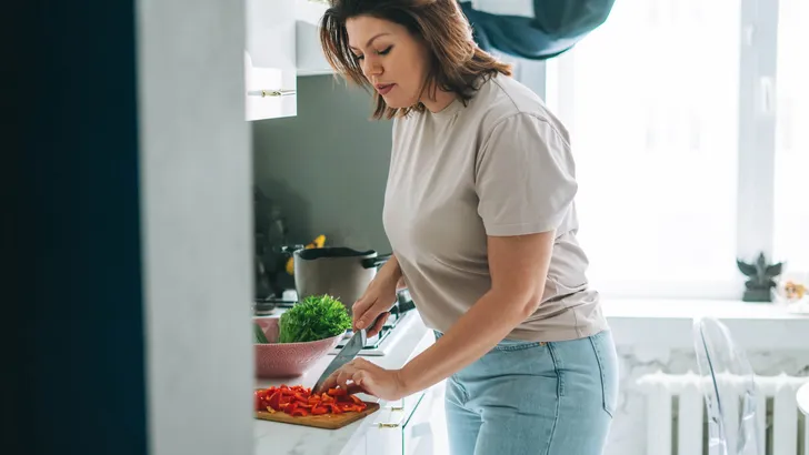 Beautiful brunette young woman plus size body positive cooking salad in kitchen at the home