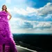 Heleen van Royen in paarse jurk op dak met lucht en wolken op achtergrond