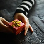 Top view of male and female hands holding gift box with ribbon on wooden background. Present for birthday, valentine day, Christmas, New Year. Congratulations background copy space.