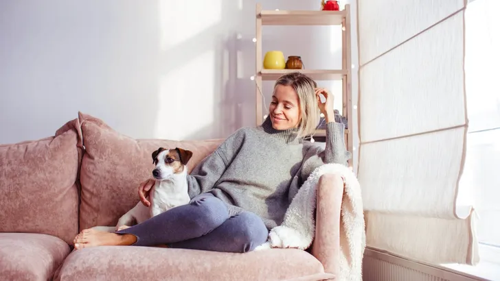 Beautiful middle-aged woman with dog at home sitting on couch