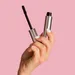 Vrouwenhand die mascara vasthoudt op roze achtergrond - waterproof