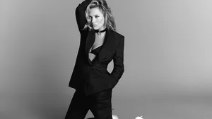 Zwart-wit foto van model Kate Moss knielend in een zwart pak tegen een grijze achtergrond. Campagnebeeld voor Elisabetta Franchi SS25.