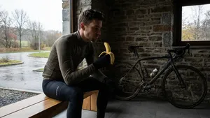 mannelijke wielrenner zit op een bankje in zijn garage en kijkt naar een afgepelde banaan, met een racefiets op de achtergrond