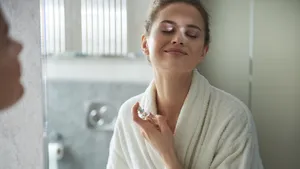 Foto van vrouw bij spiegel die parfum opspuit. Geur heeft een invloed op je humeur en deze parfums kunnen je een boost geven.