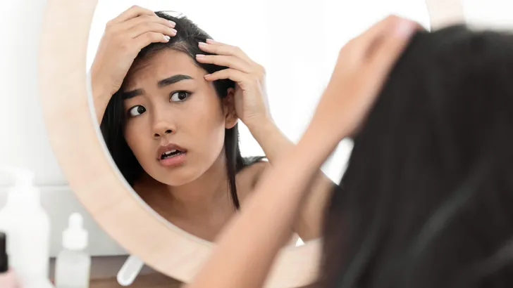 Worried asian woman checking her hair in mirror at home