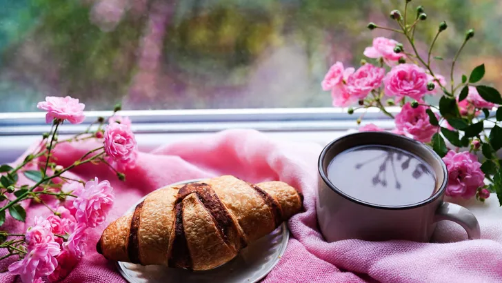 sweet fresh morning coffee and croissant staying on the windowsill with pink flowers