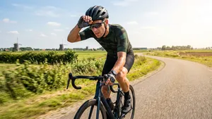 Wielrenner op de racefiets veegt met zijn handschoen het zweet van zijn voorhoofd op een warme zomerdag.
