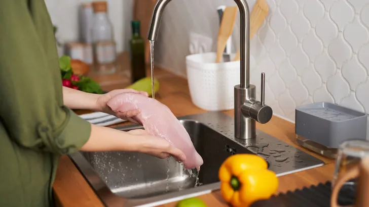Vrouw is rauwe kip aan het wassen onder de kraan