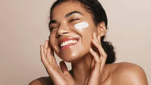 Smiling woman using skincare product. Female taking face cream to apply on facial skin