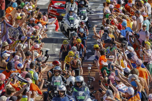 Favorietengroep Tour de France met gele trui tussen een haag van oranje geklede mensen op een berg.