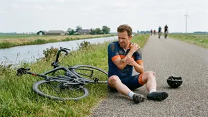Mannelijke recreatieve wielrenner zit zonder helm verslagen naast zijn racefiets na een valpartij op het asfalt.