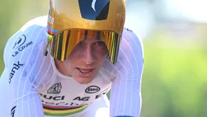 Remco Evenepoel in tijdritpositie, laag op de fiets met gouden helm en intensieve blik, vol op snelheid aan het fietsen.