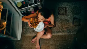 Woman eating in front of the refrigerator in the kitchen late night