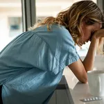 Side view of emotionally stressed mid adult woman standing in the kitchen next to a blister of pills