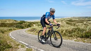 Een close-up verticaal shot van een wielrenner op een racefiets, rijdend door de duinen van een Waddeneiland op een zonnige dag.