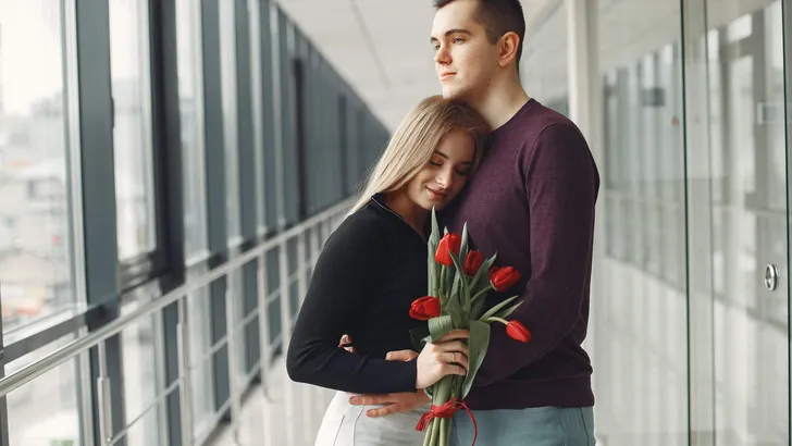 European couple is standing in a hall with a bunch of red tulips