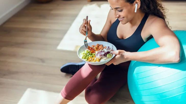 Sporty young woman eating healthy while listening to music sitti