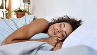 Young African American woman sleeping in modern bedroom with eyes closed.