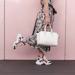 Stylish woman with a white bag in a vintage dress with fashionable sneakers posing near the pink wall. Close-up. The concept of shopping