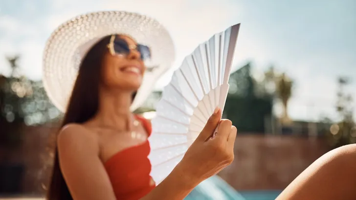 Close up of woman using hand fan during summer day by the pool.