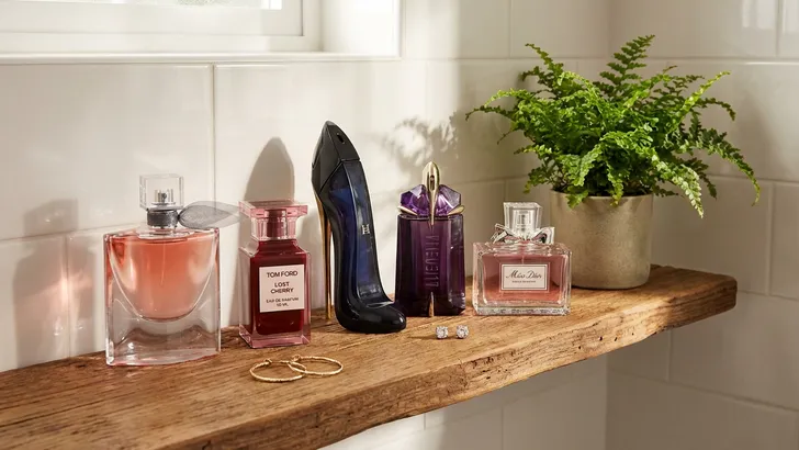 Badkamerplankje met designerparfums, oorbellen en een plantje.