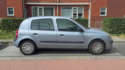 Oudere zilvergrijze Renault Clio geparkeerd langs een straat met bakstenen huizen.