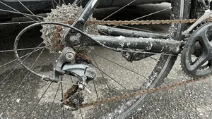 Close-up van een zwaar vervuilde en verroeste racefiets aandrijflijn, bedekt met modder en witte pekelresten na een winterrit.